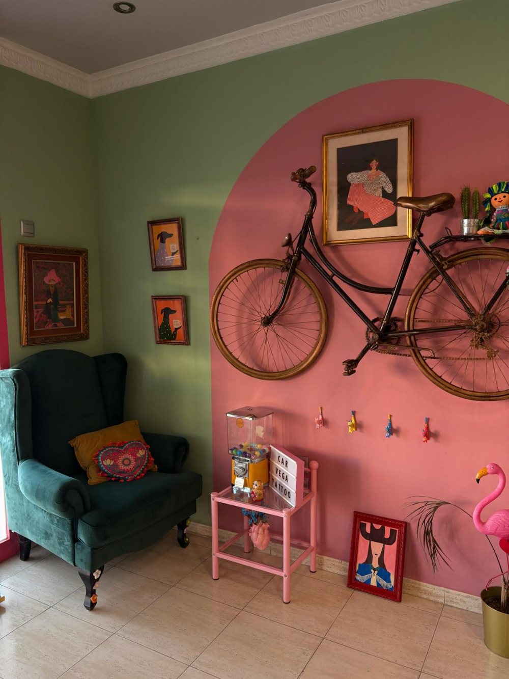 Rincón del estudio con un arco pintado de rosa, una bicicleta antigua colgada y un sillón de terciopelo verde
