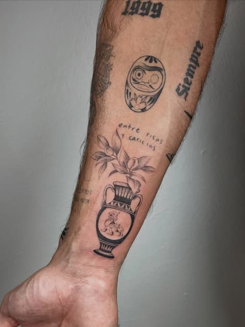 Antebrazo con un daruma, un jarrón con flores y lettering