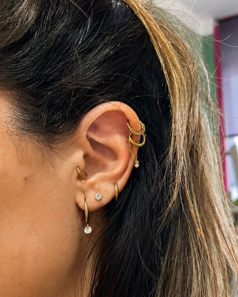 Oreja con varios aros y pendientes dorados en el cartílago y el lóbulo