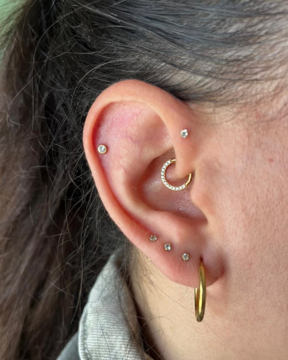 Oreja con un piercing de daith con brillantes y varios puntos de luz en el cartílago y el lóbulo